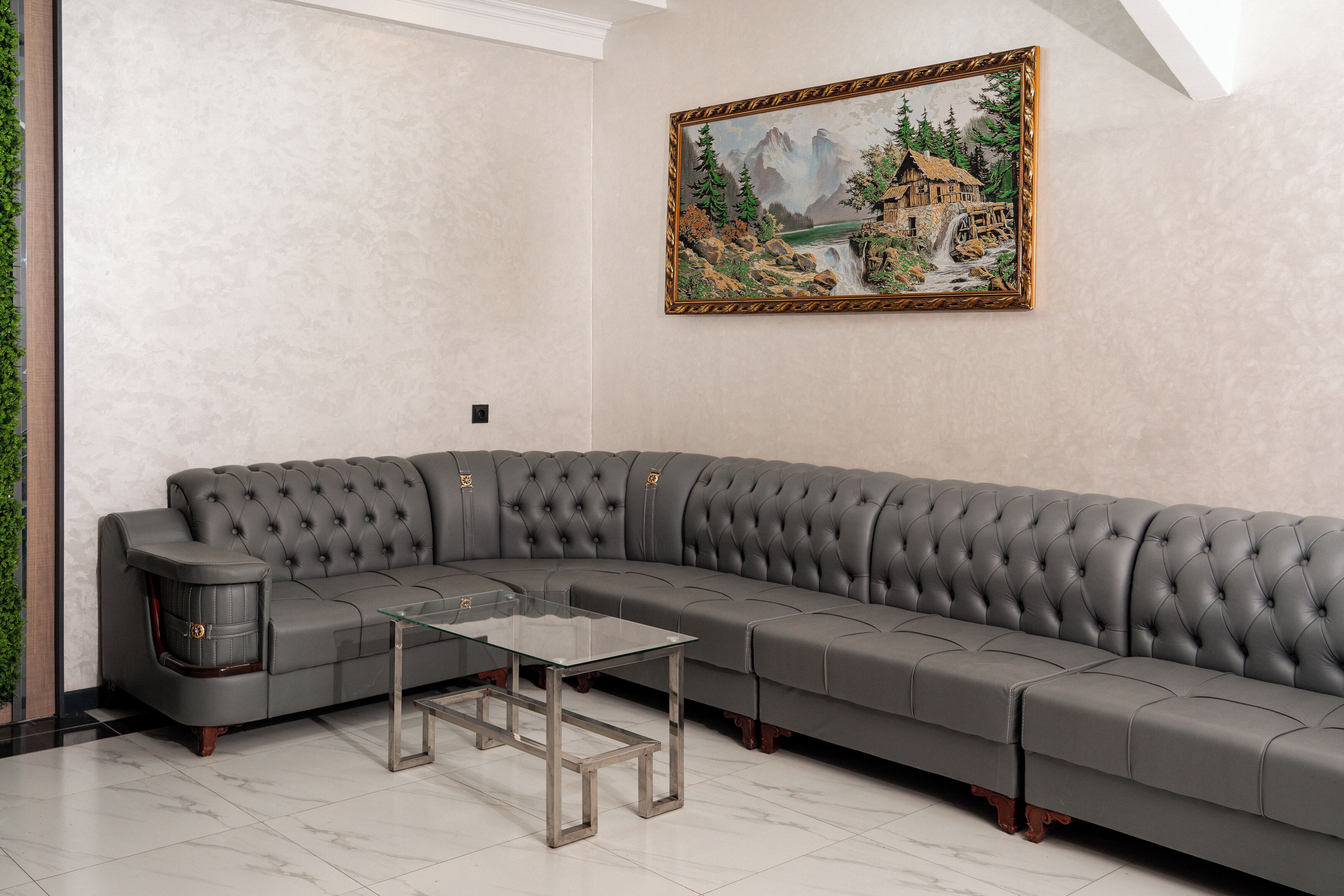 Un sofá seccional gris con una mesa de centro de vidrio en una habitación con un cuadro en la pared.