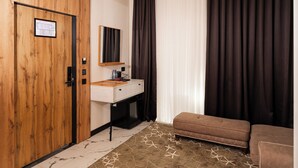 A room with a wooden wardrobe, a white desk with a mirror, a brown sofa, and patterned flooring. - Gulshan Hotel (Urgench)