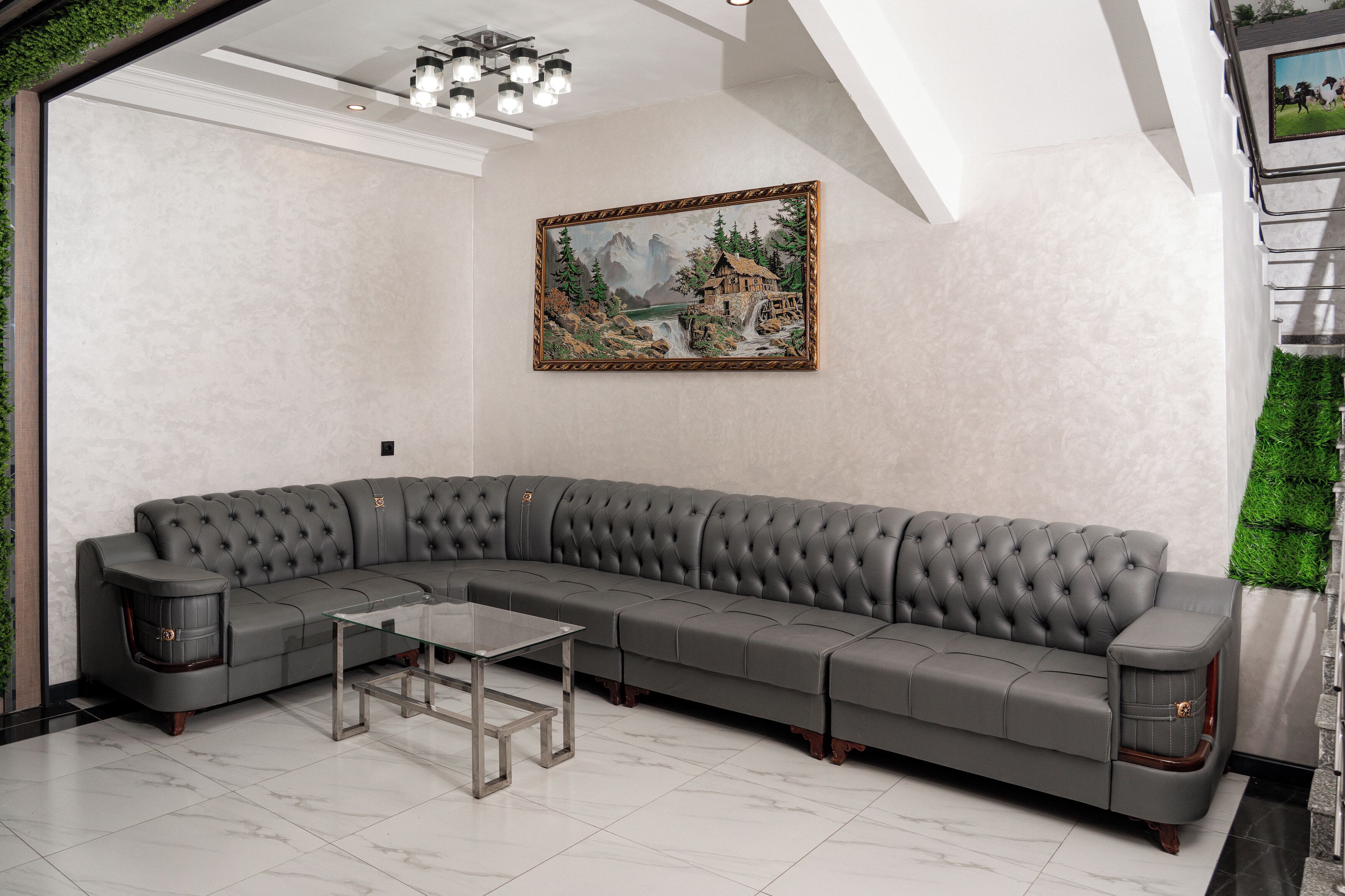 A modern living room with a grey sectional sofa, a glass coffee table, and a framed landscape painting on the wall.