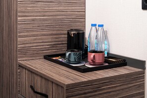 A wooden cabinet with a tray containing a coffee maker, two water bottles, and two cups. - Gulshan Hotel (Urgench)