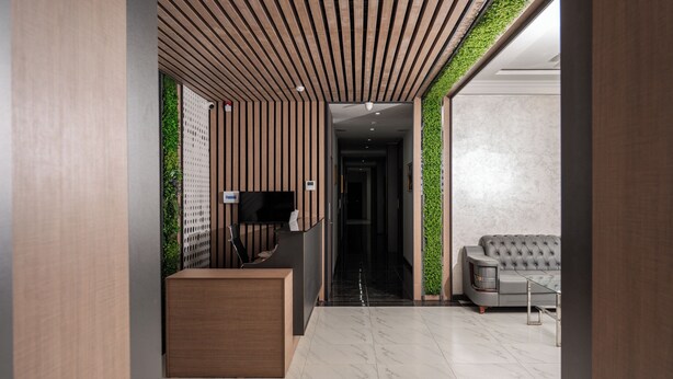 A modern interior with a reception desk, a flat-screen TV, a sofa, and a green wall. - Gulshan Hotel (Urgench)
