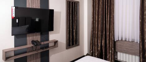 A hotel room with a bed, a mounted television, a telephone, and a window with curtains.