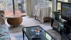 A living room with a ceiling fan, a television, a dog, a coffee table, a sofa, and a large window with a view of the outdoors. - Cozy 2-bedroom house in amazing Myrtle Beach with AC (Myrtle Beach)