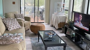 A living room with a sofa, ottoman, coffee table, television, and a ceiling fan. - Cozy 2-bedroom house in amazing Myrtle Beach with AC (Myrtle Beach)