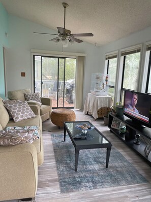 A living room with a sofa, ottoman, coffee table, television, and a ceiling fan. - Cozy 2-bedroom house in amazing Myrtle Beach with AC (Myrtle Beach)
