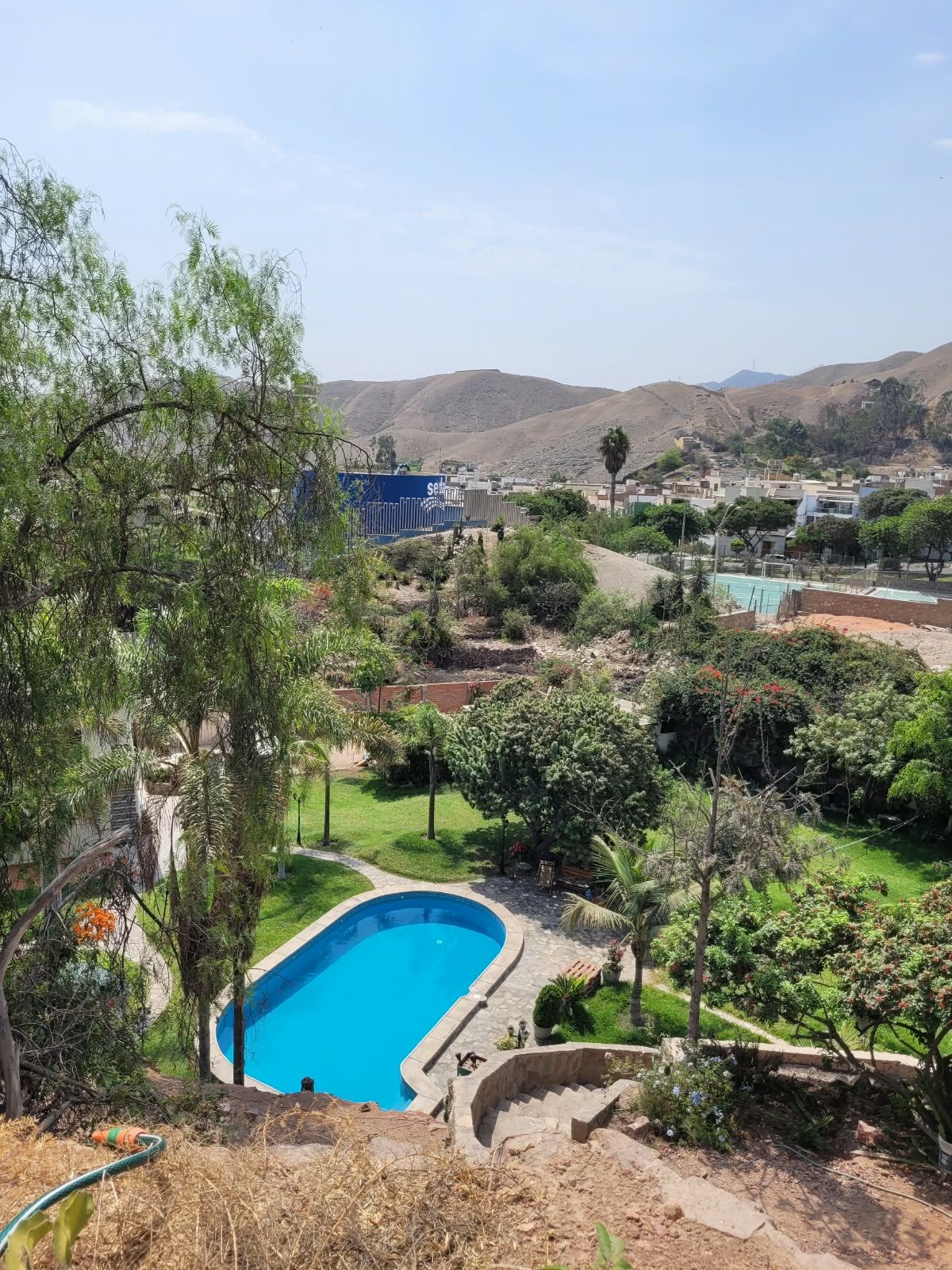 Un quartier résidentiel doté d’une piscine entourée de verdure et offrant une vue sur des collines lointaines.