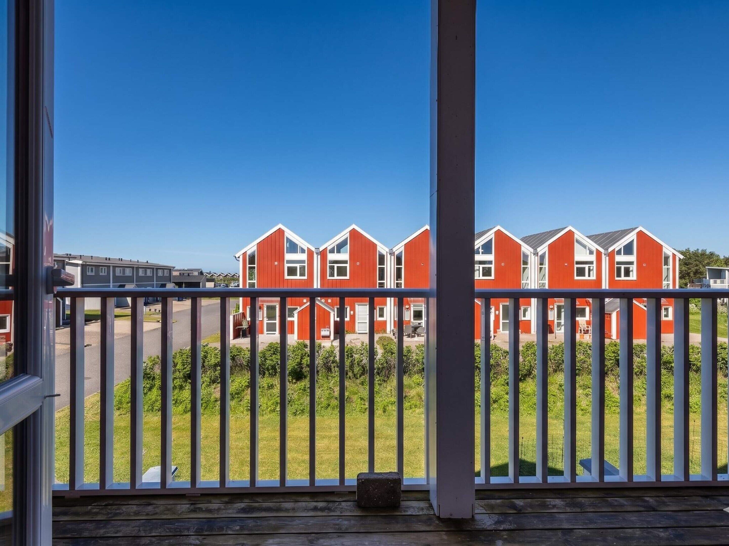 Una hilera de casas rojas con detalles blancos, una terraza de madera y un cielo azul despejado.