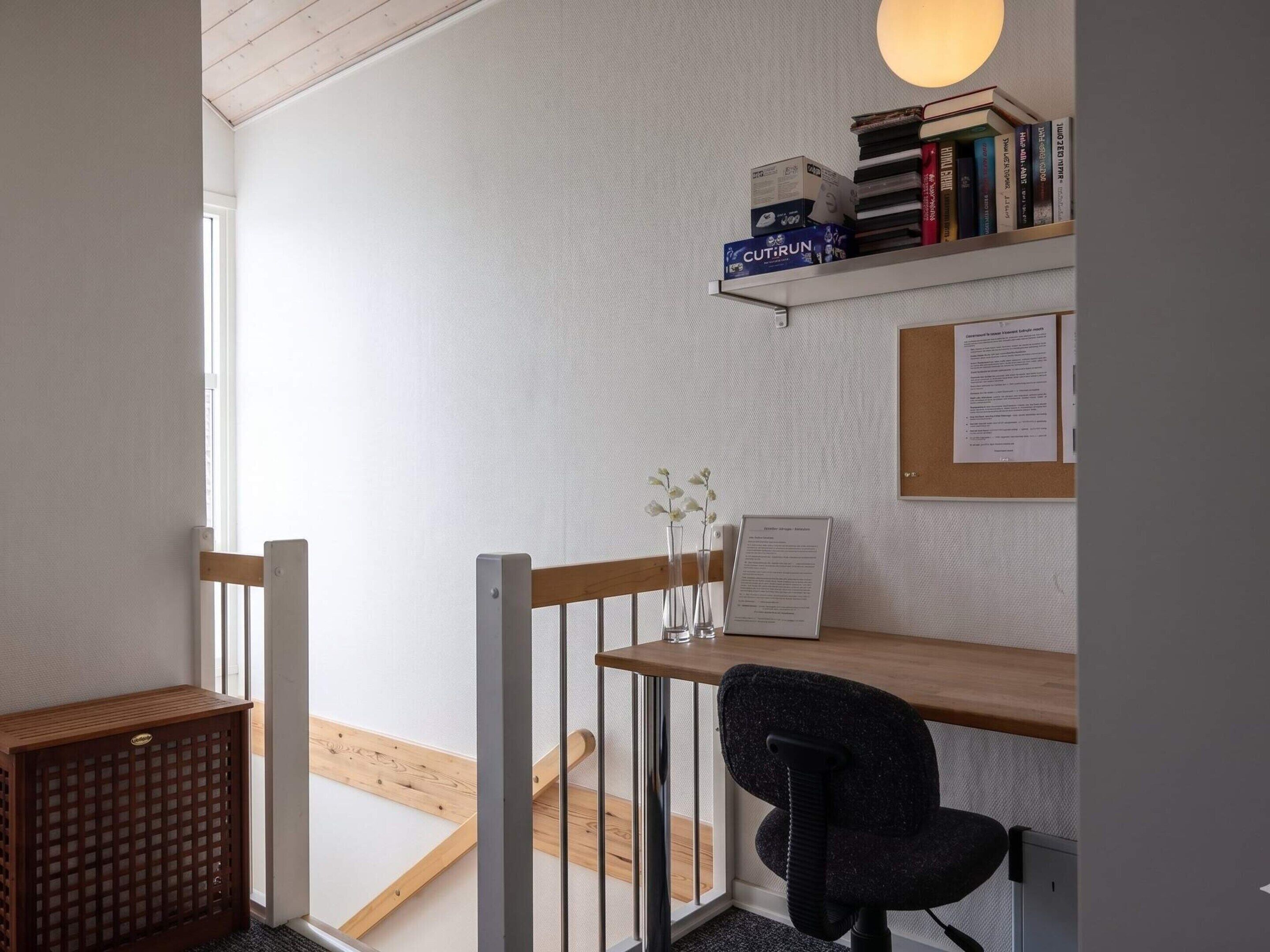 Een werkplek met een bureau, stoel en boekenplanken met boeken en een lamp.