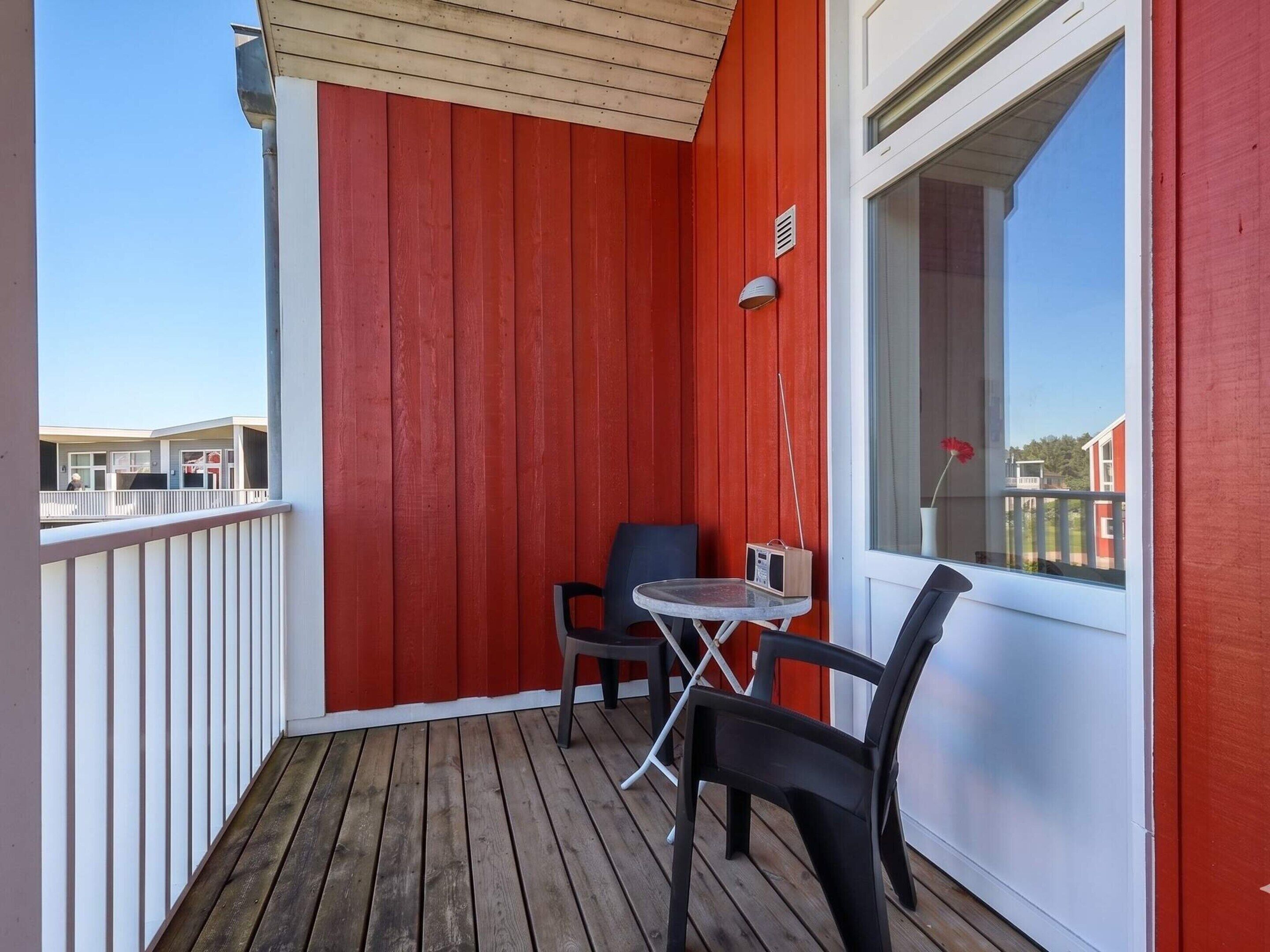 En balkon med rød væg, et lille bord med stole og et vindue.