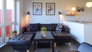 Et moderne opholdsområde med en sofa, et sofabord og et køkken med vask og redskaber.