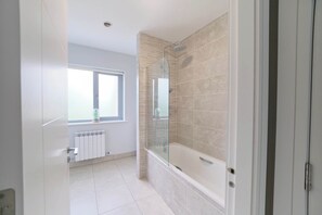 A modern bathroom with a glass-enclosed shower, a bathtub, and a window providing natural light.