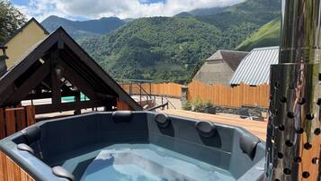 Un bain à remous avec une terrasse en bois et une vue sur les montagnes en arrière-plan.