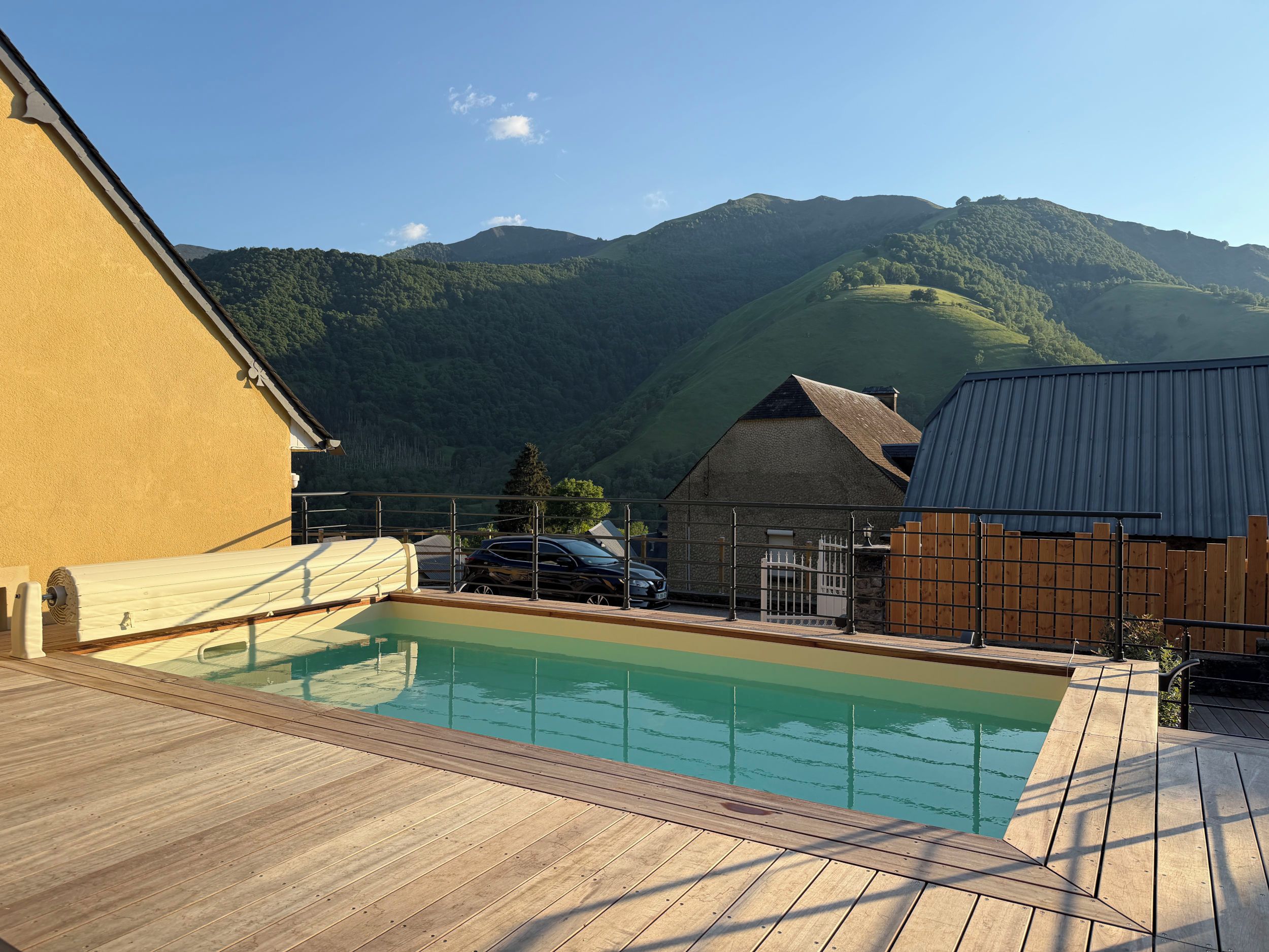 Une terrasse en bois avec une piscine, un bâtiment en pierre et une vue sur les montagnes en arrière-plan.