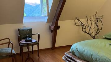 Une chambre avec un plafond en pente, une fenêtre donnant sur les montagnes, un lit recouvert d’une couverture verte, une chaise agrémentée d’un coussin décoratif et un plancher en bois.