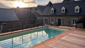 A swimming pool with a wooden deck, surrounded by stone buildings with pitched roofs. - Rental: Gazost Fountains (Gazost)