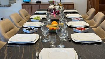 Une table à manger dressée pour un repas, avec des assiettes, des couverts et des verres, entourée de chaises.