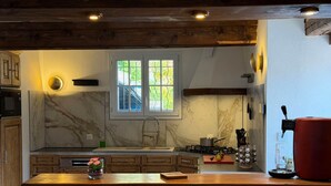 A kitchen with a stone countertop, wooden cabinets, a window, and a red appliance. - Rental: Gazost Fountains (Gazost)
