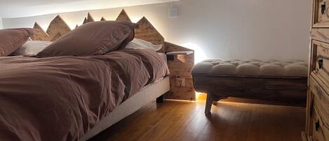 Een slaapkamer met een bed, nachtkastje, houten dressoir en een raam.