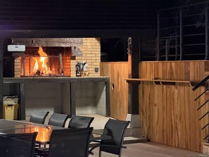 An outdoor dining area with a brick fireplace, a wooden fence, and a metal staircase.