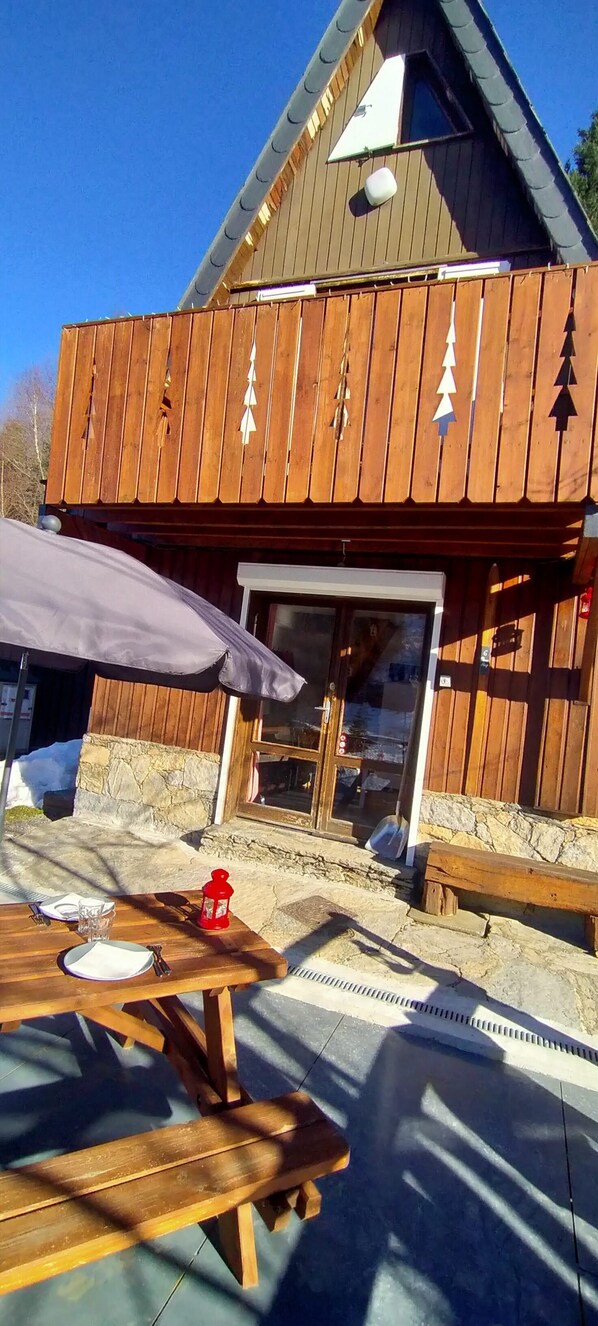 Un bâtiment en bois avec des fondations en pierre, une terrasse en bois et une table avec des sièges pour l’extérieur.
