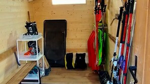 A wooden interior with a ceiling, a shelf with boots, a mat, and skis.