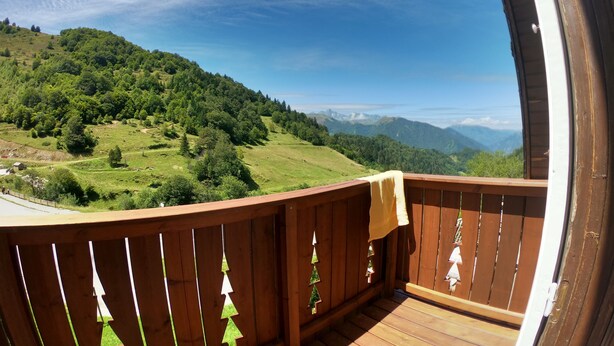 A balcony with a view of a green hillside and distant mountains.
