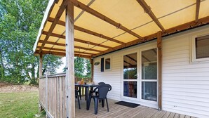 En inglasad veranda med ett bord och stolar, ett träräcke och ett hus med stora fönster.