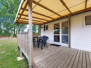 A covered deck with a table and chairs, wooden railing, and a house with large windows. - Le Kernic 2 by Interhome (Plouescat)