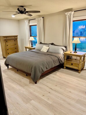 Une chambre à coucher avec un lit, deux tables de chevet, un ventilateur de plafond et une vue par la fenêtre.