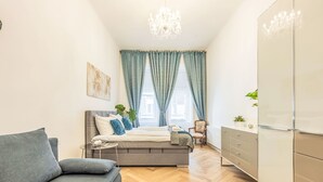Een moderne slaapkamer met een bed, een grijze bank, een dressoir en een kroonluchter.