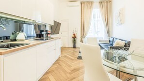 Een moderne keuken met een flatscreen-tv, een koffieapparaat en een eethoek met een glazen tafel en witte stoelen.