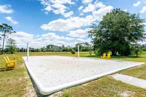 Un terrain de volley-ball avec un filet, entouré d’herbe et d’arbres.