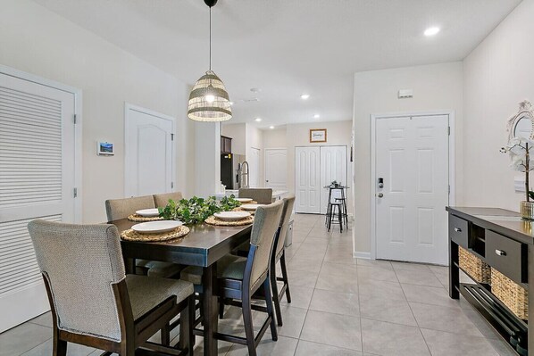 A dining area with a table set for four, surrounded by chairs, a hanging light fixture, and a view into the kitchen. - Tropical Oasis 2 bdr - patio, playground, dog park (Jacksonville)