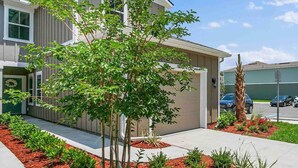 Uma casa moderna de dois andares com um jardim da frente bem cuidado, incluindo uma pequena árvore e várias plantas.