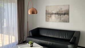 Una sala de estar moderna con un sofá de cuero negro, una mesa de centro blanca, una lámpara de pie y un cuadro en la pared.