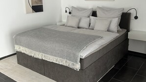 Un dormitorio moderno con una cama grande, una mesita de noche, una lámpara de pared y un cuadro abstracto en la pared.