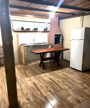Una cocina con un horno de ladrillo, un refrigerador blanco y una mesa de madera.