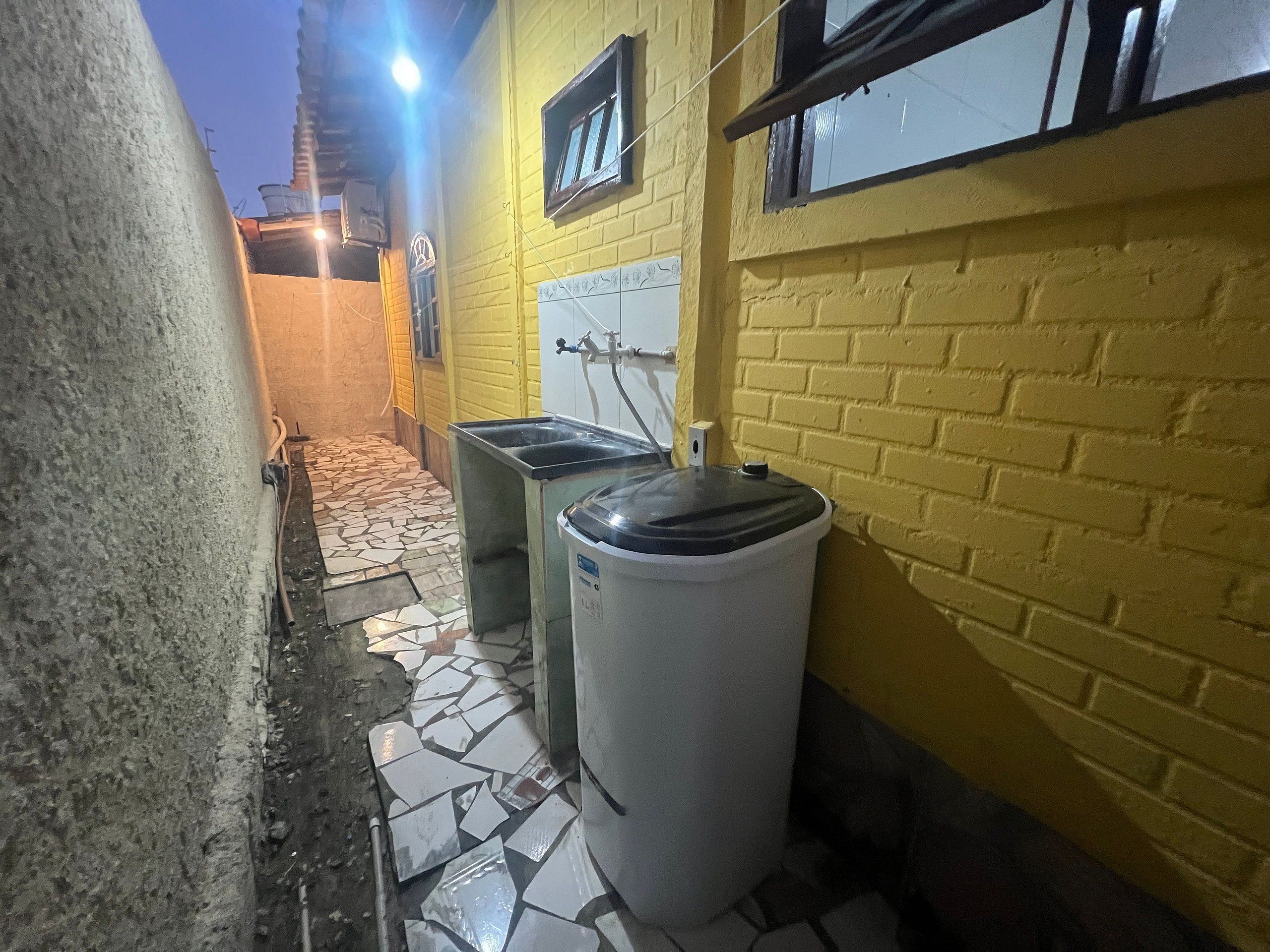 A narrow alley with a tiled floor, a yellow brick wall, and a white trash bin.