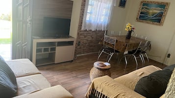 Uma sala de estar mobiliada com sofá, televisão, mesa de jantar com cadeiras e um quadro decorativo na parede.