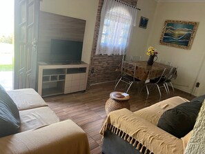Uma sala de estar mobiliada com sofá, televisão, mesa de jantar com cadeiras e um quadro decorativo na parede.