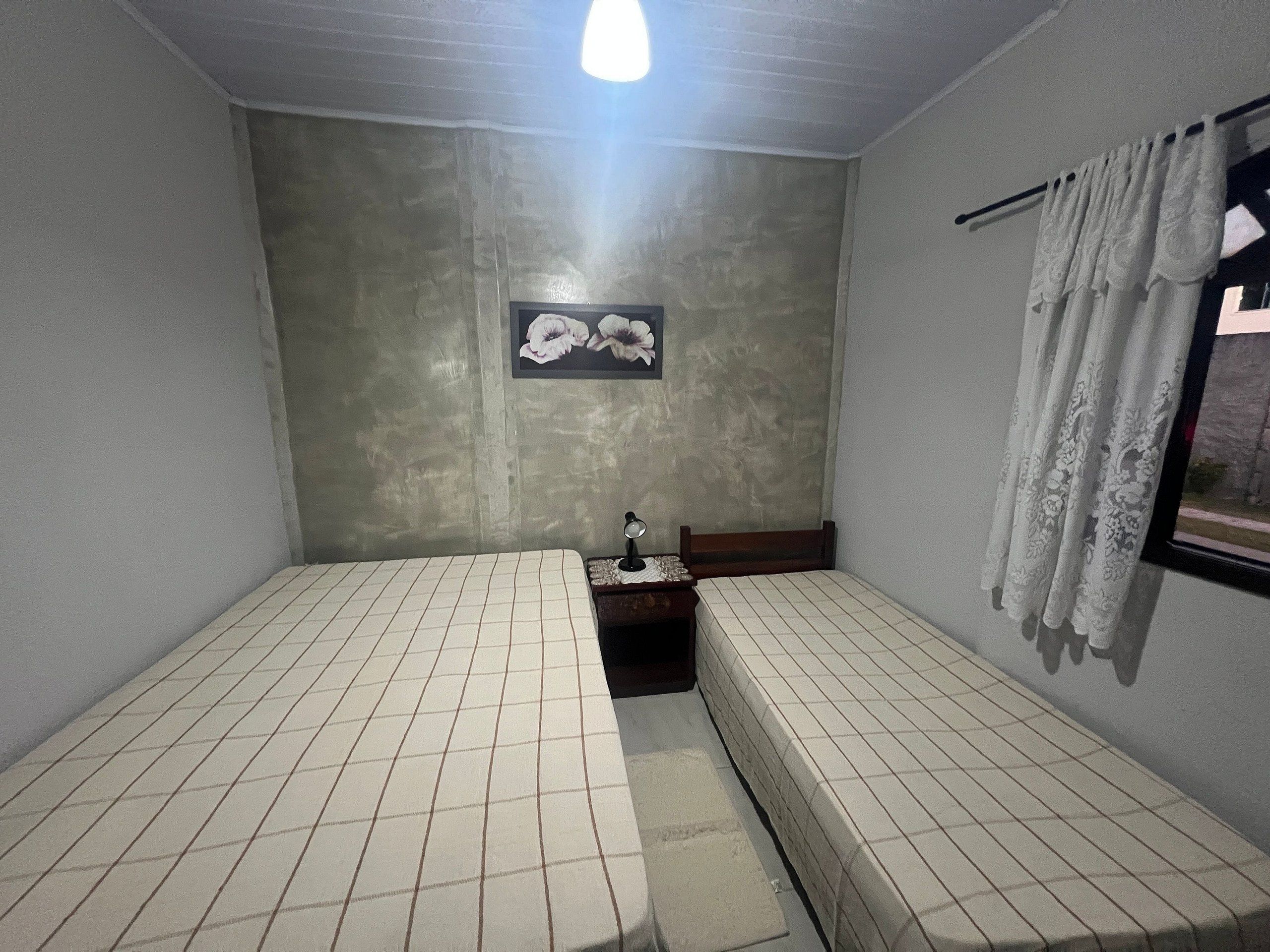 Een kamer met twee eenpersoonsbedden, een klein tafeltje met een lamp, een foto aan de muur en een raam met gordijnen.