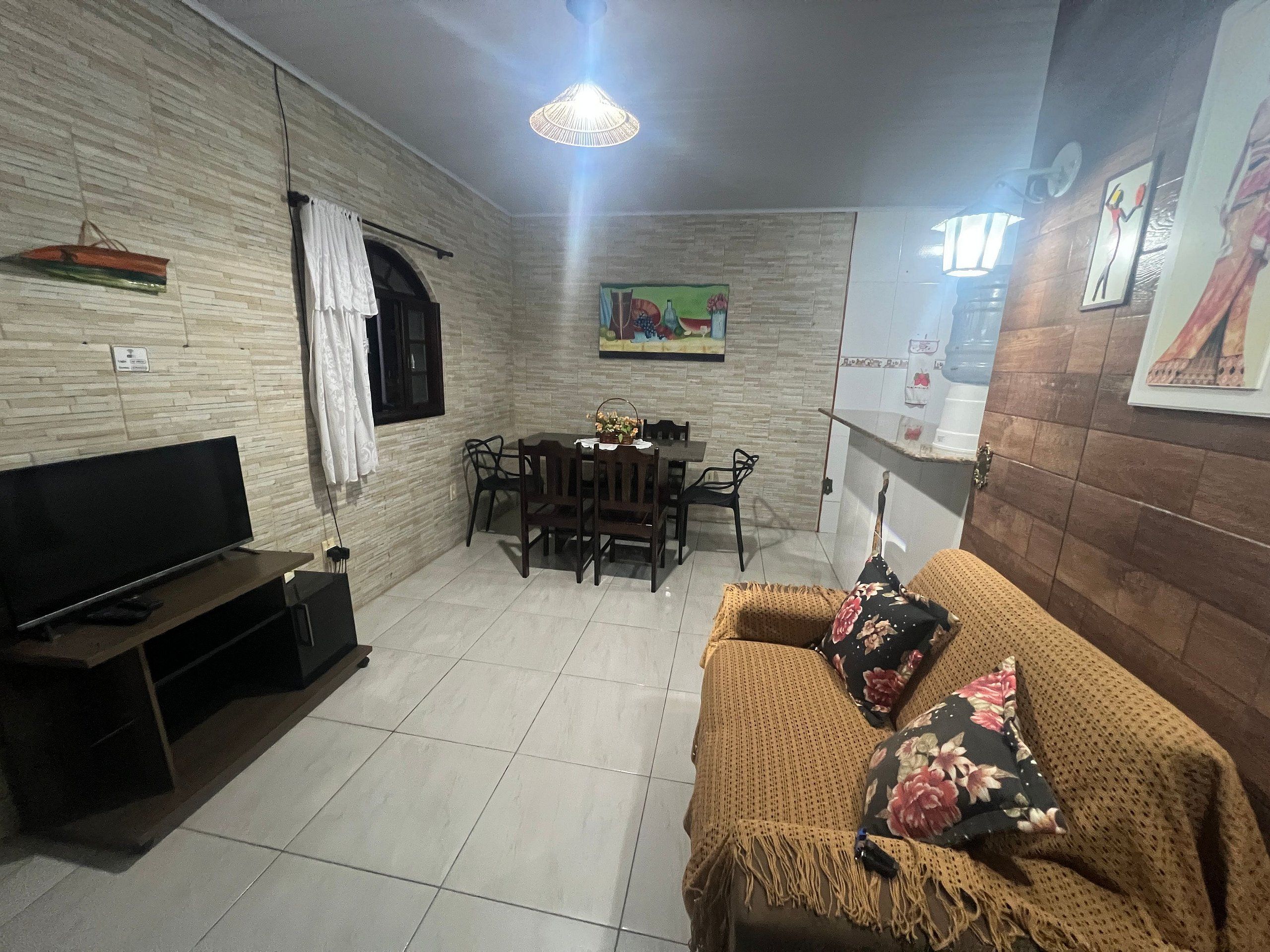 A living room with a flat-screen TV, a sofa, a dining table with chairs, and a painting on the wall.