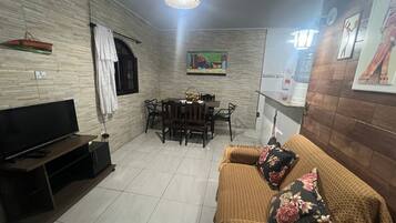 A living room with a flat-screen TV, a sofa, a dining table with chairs, and a painting on the wall.