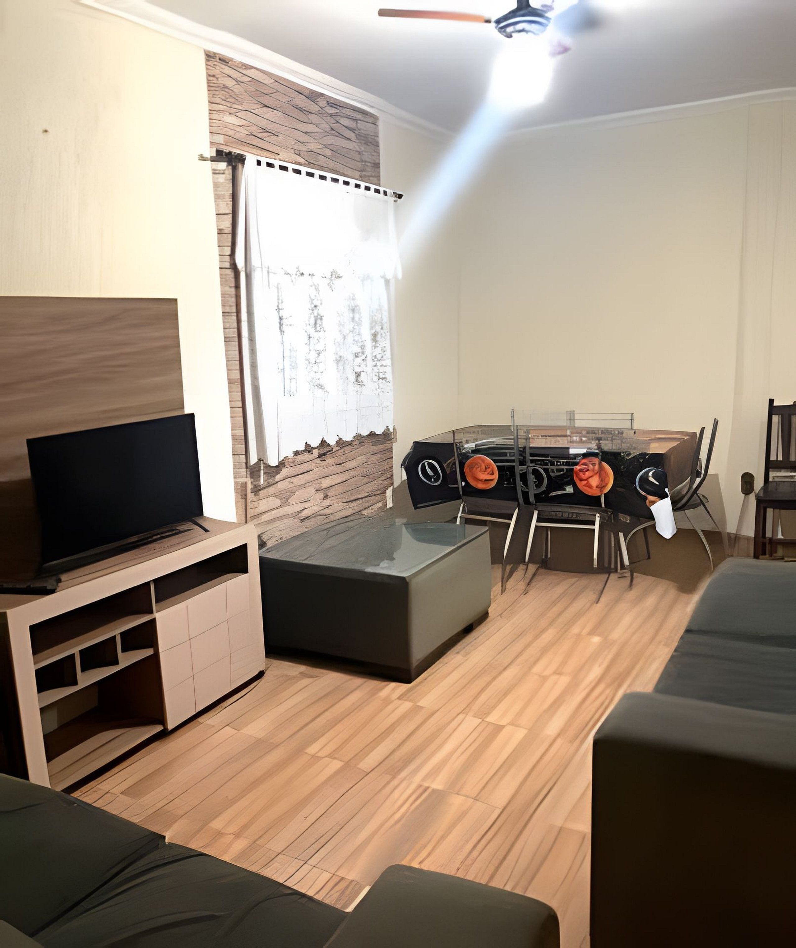 A living room with a flat-screen TV, a sofa, a dining table with chairs, and a ceiling fan.