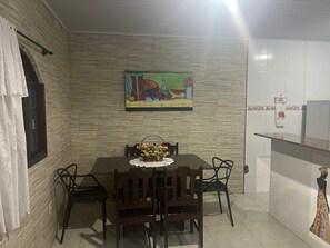 Uma área de refeições com uma mesa, cadeiras, um quadro e uma geladeira.