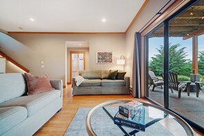 A modern living room with a sofa, a glass coffee table, and a view of outdoor patio furniture through large windows. - Cabin with Sauna & Cold Plunge, 8 people + kids (Salt Spring Island)