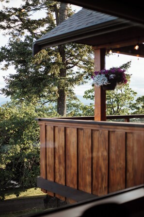 A wooden deck with a railing, overlooking a natural landscape with trees and a body of water. - Cabin with Sauna & Cold Plunge, 8 people + kids (Salt Spring Island)