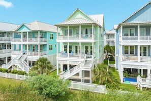 A multi-story beachfront hotel with balconies, a pool, and a white picket fence. - Drift Away to the Beach - 5BR Beachside Home with Elevator & Easy Beach Access (Galveston)