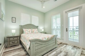 Ein Schlafzimmer mit Bett, Nachttischen, Deckenventilator und einer Tür zum Balkon.