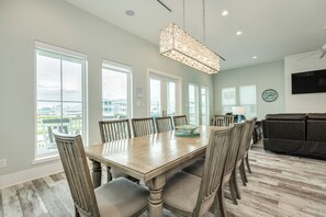 A dining area with a large wooden table, chairs, and a hanging light fixture. - Drift Away to the Beach - 5BR Beachside Home with Elevator & Easy Beach Access (Galveston)